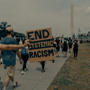 man in gray t-shirt holding black and white welcome to the beach signage